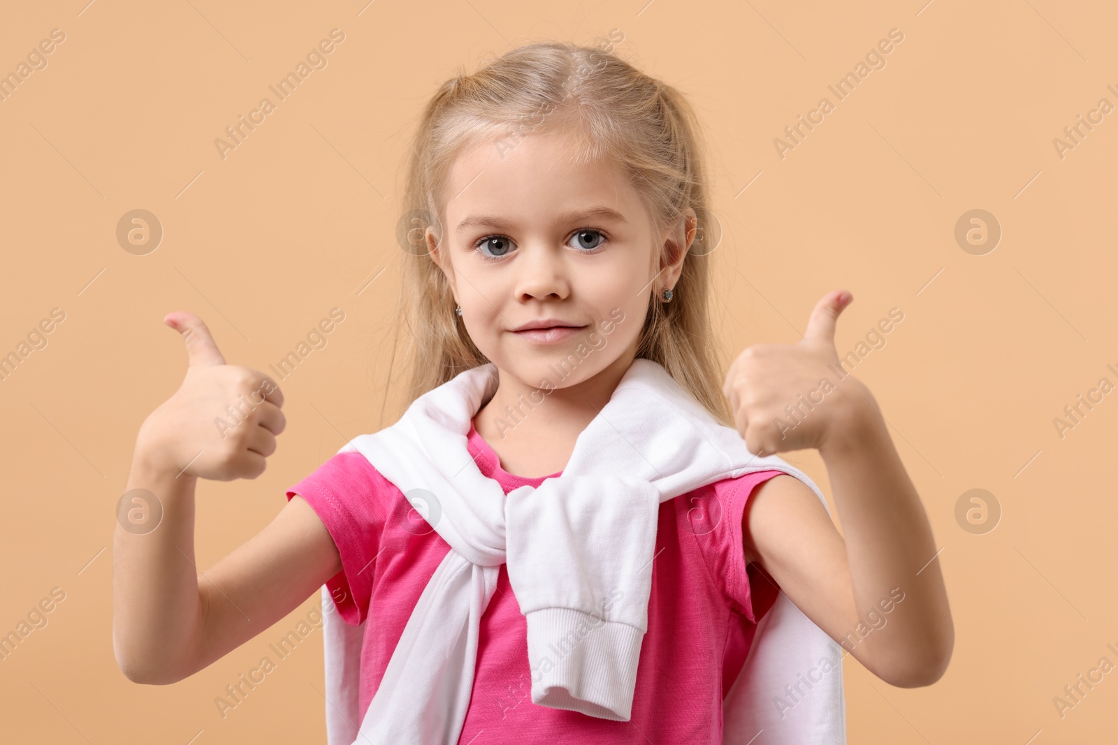 Photo of Cute little girl showing thumbs up on beige background