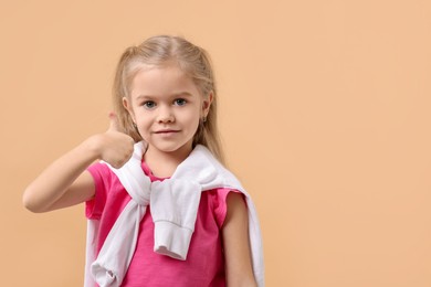 Photo of Cute little girl showing thumbs up on beige background, space for text