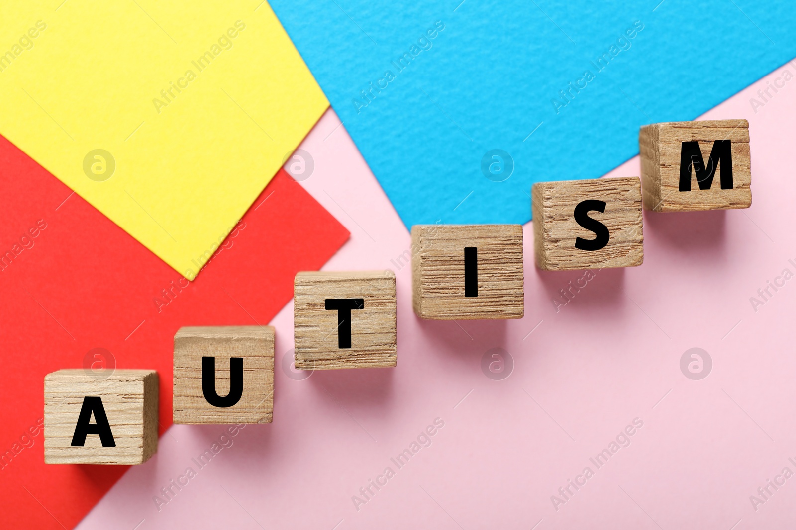 Photo of Word Autism made with wooden cubes and colorful sheets of paper on pink background, flat lay