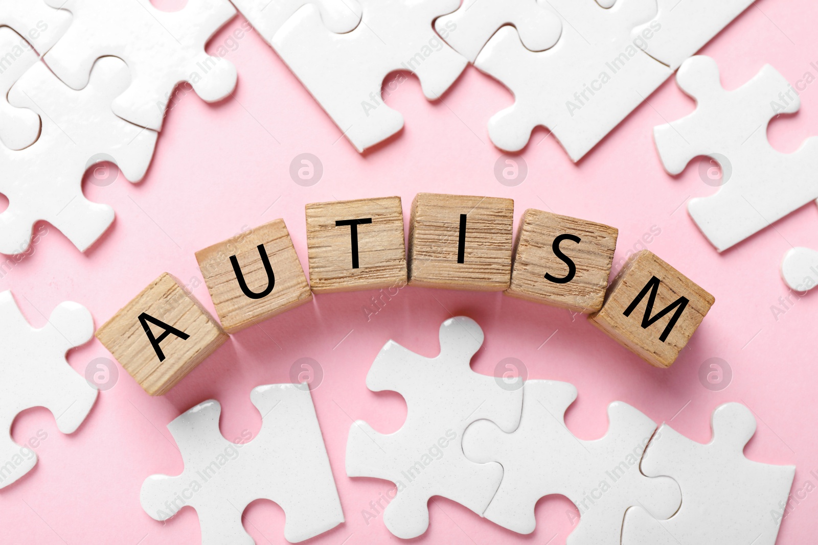 Photo of Word Autism made with wooden cubes and puzzle pieces on pink background, flat lay