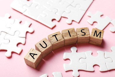 Photo of Word Autism made with wooden cubes and puzzle pieces on pink background, closeup