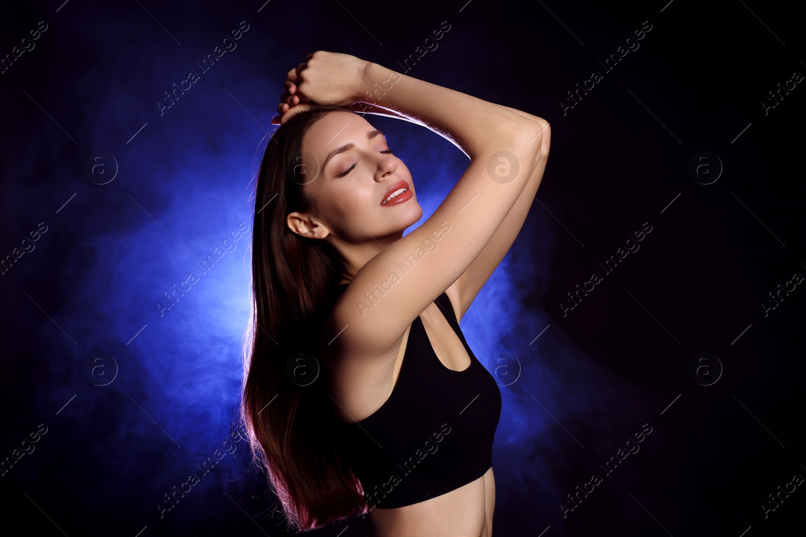 Photo of Beautiful woman in stylish sportswear on dark background with color light and smoke