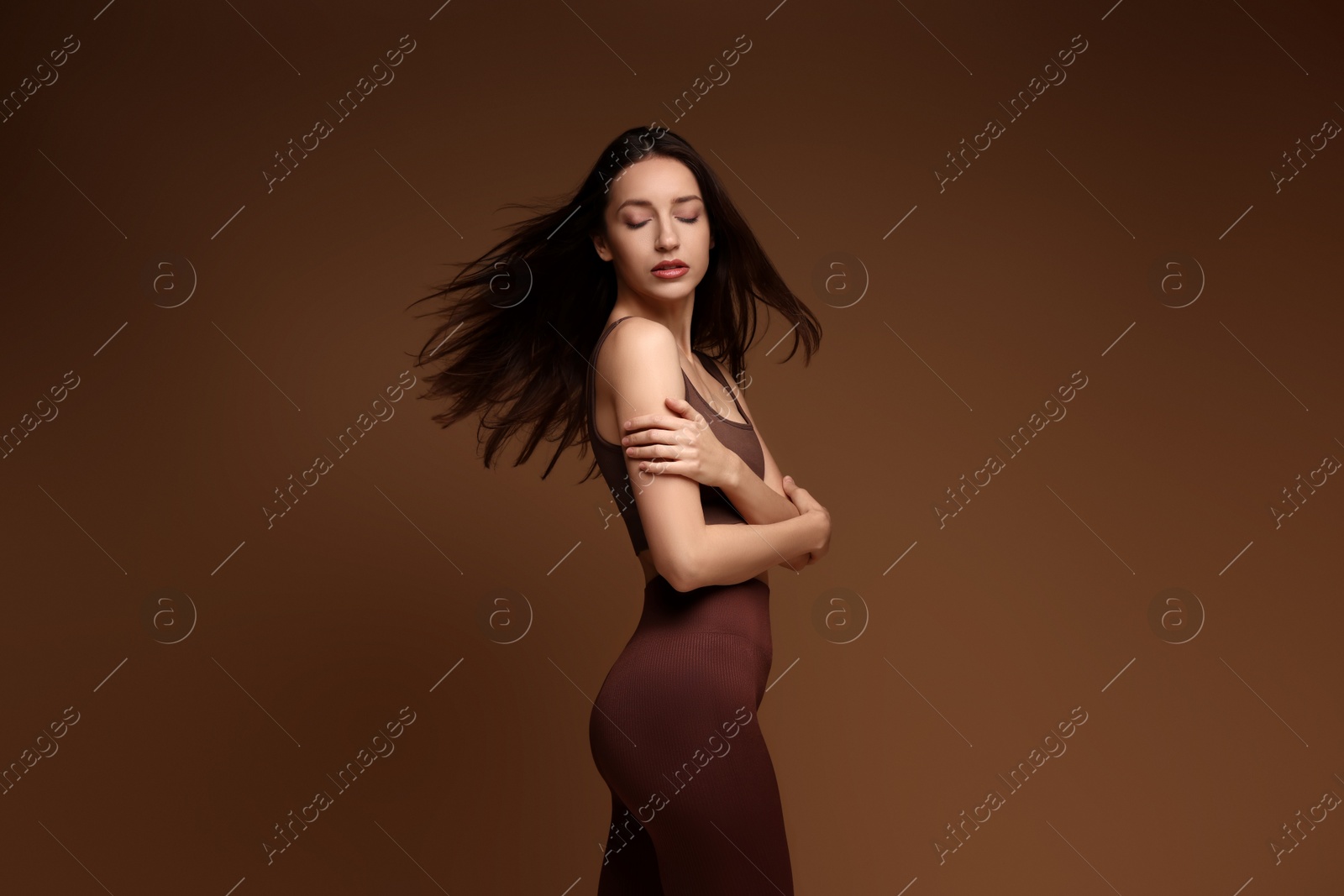 Photo of Beautiful woman in stylish sportswear on brown background