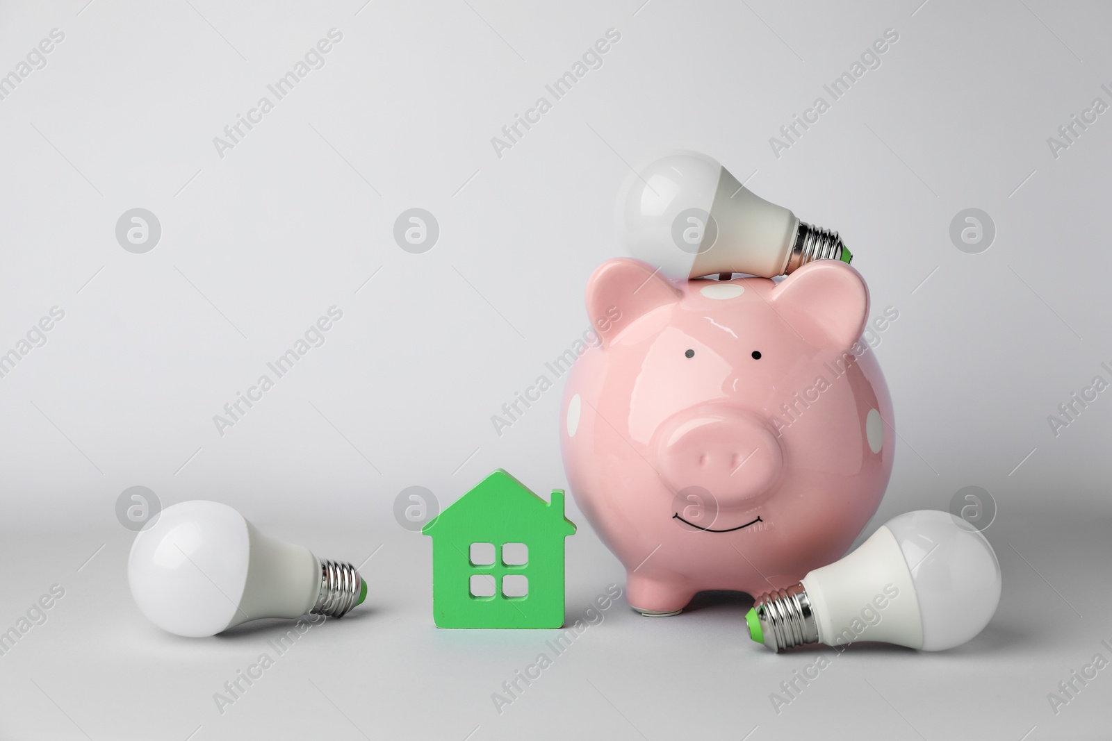 Photo of Piggy bank, house model and light bulbs on grey background. Energy saving concept