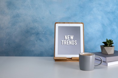 Image of New trends. Modern tablet, cup of coffee, books and succulent on white table near blue wall