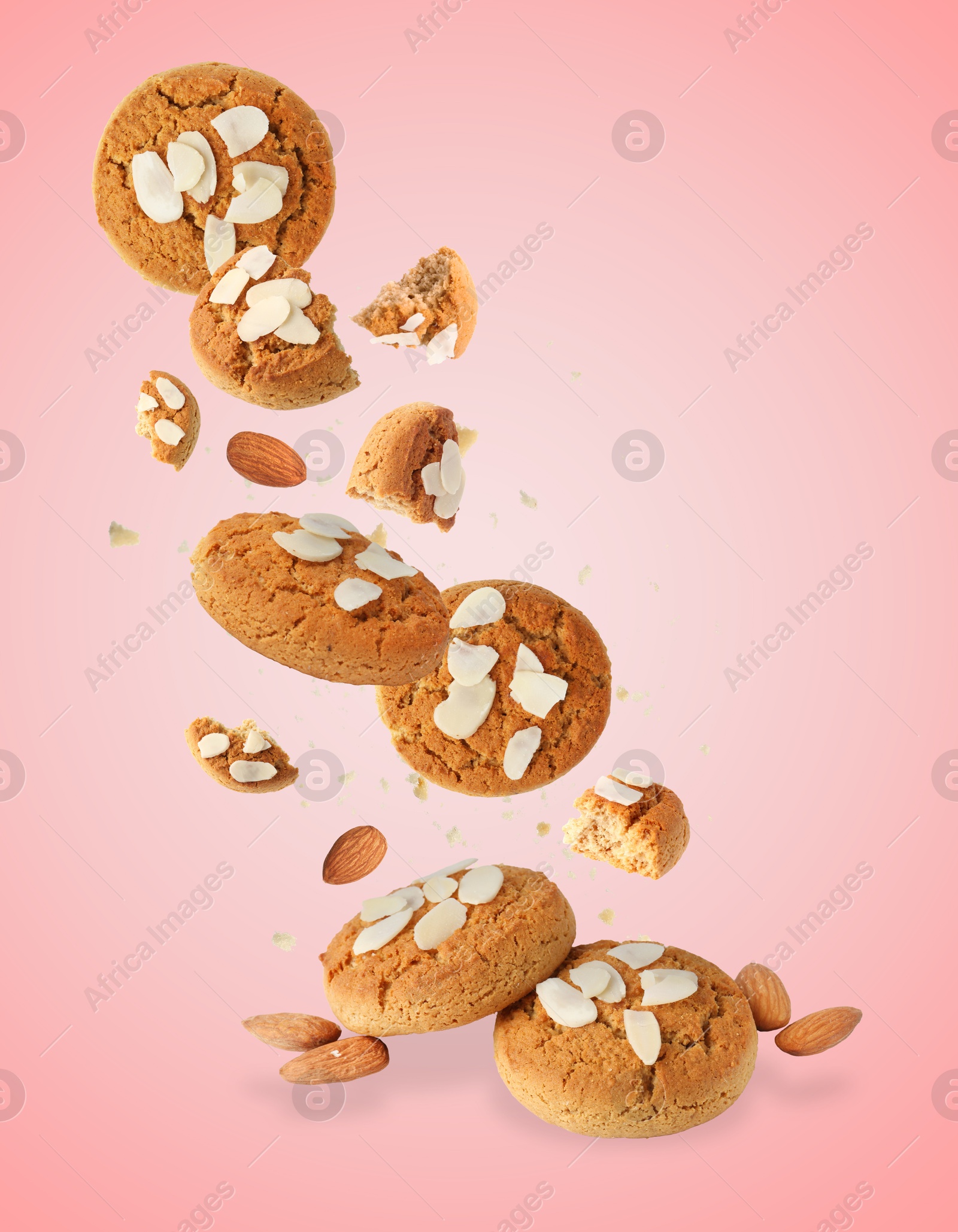 Image of Yummy nut cookies with almond petals in air on coral background