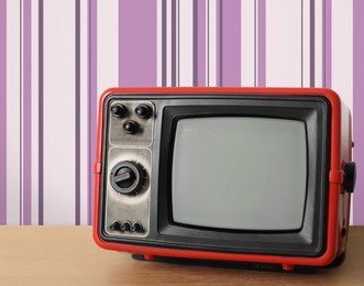 Image of Retro TV on wooden table near wall with vintage style wallpaper