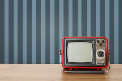 Image of Retro TV on wooden table near wall with vintage style wallpaper. Space for text