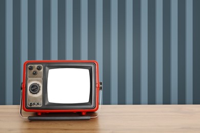 Image of Retro TV on wooden table near wall with vintage style wallpaper. Space for text