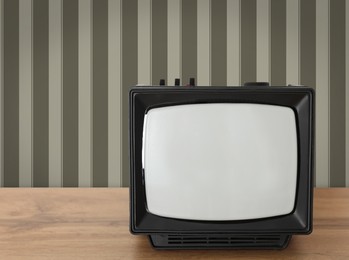 Image of Retro TV on wooden table near wall with vintage style wallpaper. Space for text