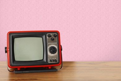 Image of Retro TV on wooden table near wall with vintage style wallpaper. Space for text