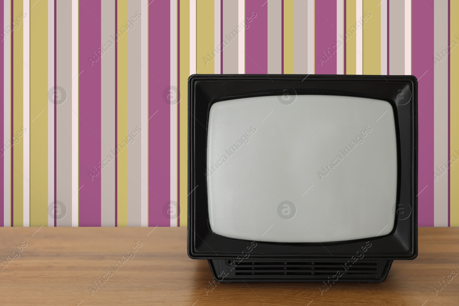 Image of Retro TV on wooden table near wall with vintage style wallpaper. Space for text