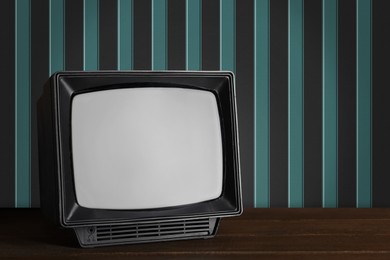 Image of Retro TV on wooden table near wall with vintage style wallpaper. Space for text