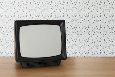 Image of Retro TV on wooden table near wall with vintage style wallpaper. Space for text