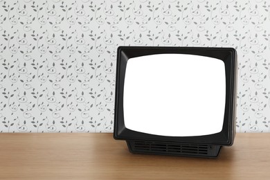 Image of Retro TV on wooden table near wall with vintage style wallpaper. Space for text