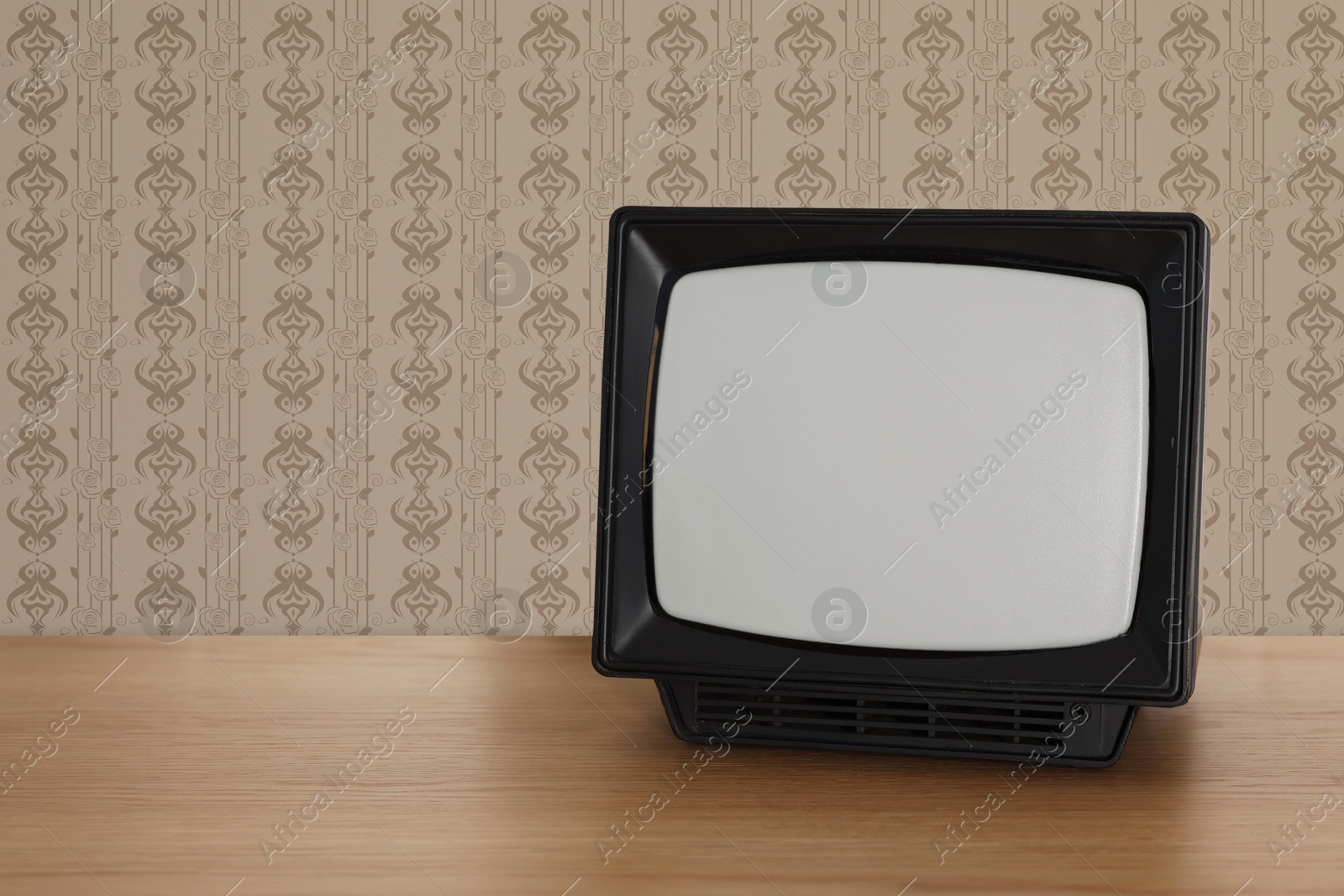 Image of Retro TV on wooden table near wall with vintage style wallpaper. Space for text