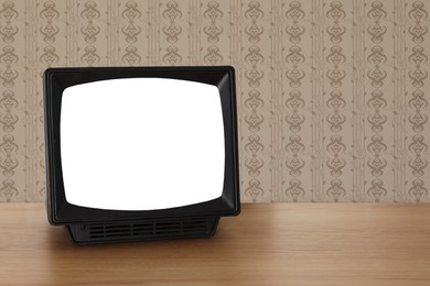 Image of Retro TV on wooden table near wall with vintage style wallpaper. Space for text