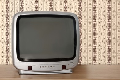 Image of Retro TV on wooden table near wall with vintage style wallpaper. Space for text