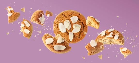 Yummy nut cookies with almond petals in air on color background