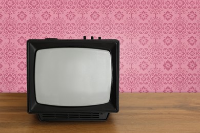 Image of Retro TV on wooden table near wall with vintage style wallpaper. Space for text