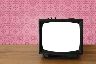 Image of Retro TV on wooden table near wall with vintage style wallpaper. Space for text