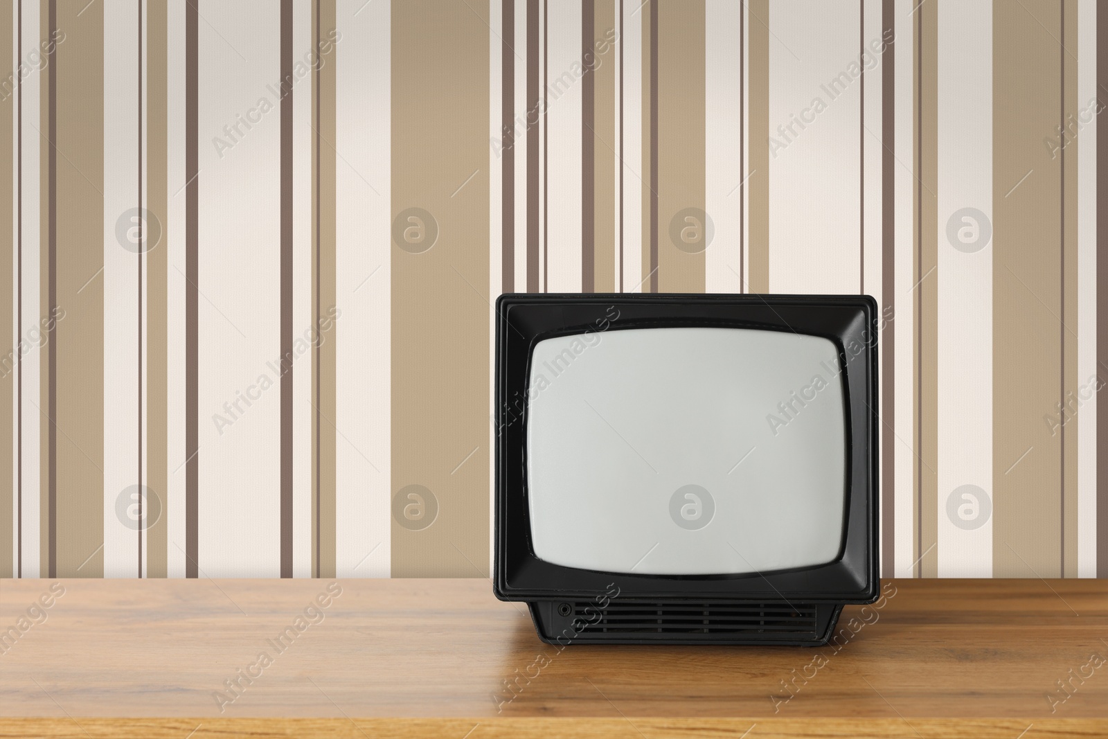 Image of Retro TV on wooden table near wall with vintage style wallpaper. Space for text