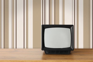 Image of Retro TV on wooden table near wall with vintage style wallpaper. Space for text