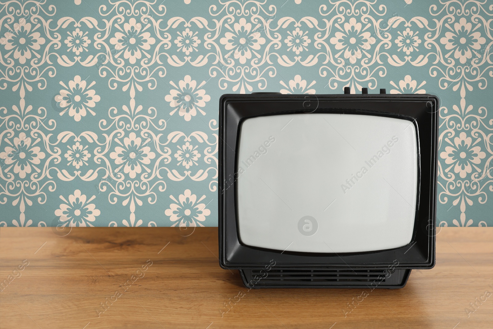 Image of Retro TV on wooden table near wall with vintage style wallpaper. Space for text