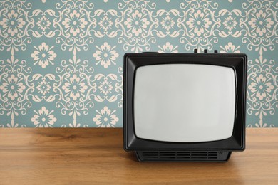 Image of Retro TV on wooden table near wall with vintage style wallpaper. Space for text