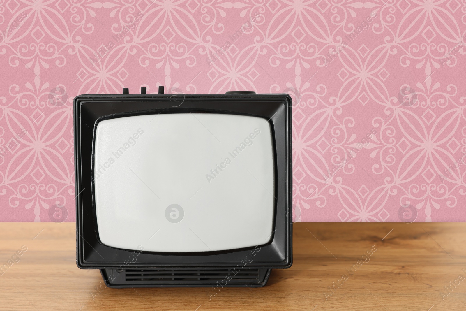 Image of Retro TV on wooden table near wall with vintage style wallpaper. Space for text