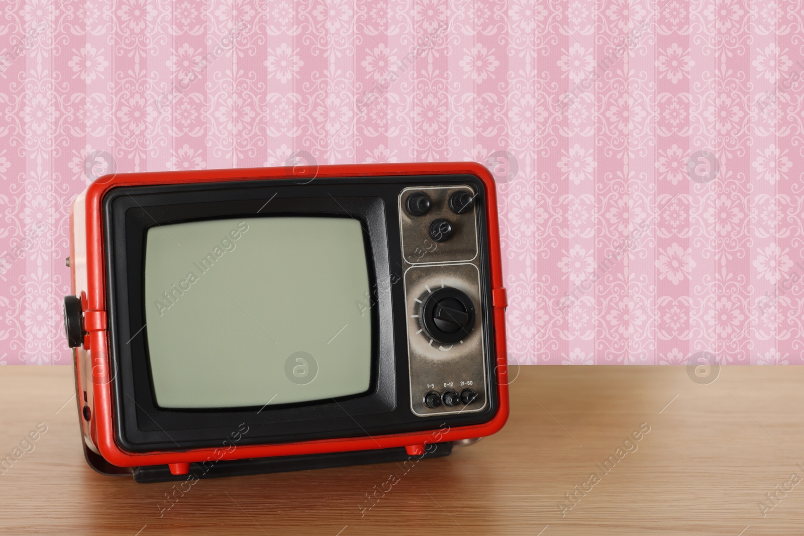 Image of Retro TV on wooden table near wall with vintage style wallpaper. Space for text