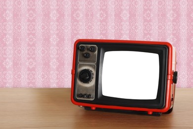 Image of Retro TV on wooden table near wall with vintage style wallpaper. Space for text