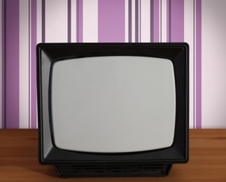 Image of Retro TV on wooden table near wall with vintage style wallpaper