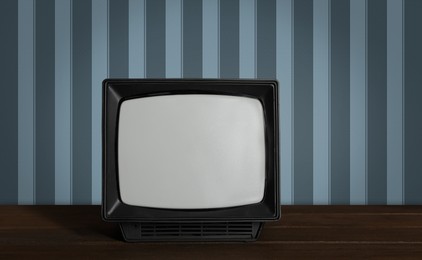 Image of Retro TV on wooden table near wall with vintage style wallpaper