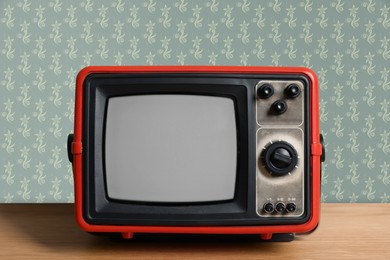 Image of Retro TV on wooden table near wall with vintage style wallpaper