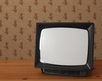 Image of Retro TV on wooden table near wall with vintage style wallpaper. Space for text