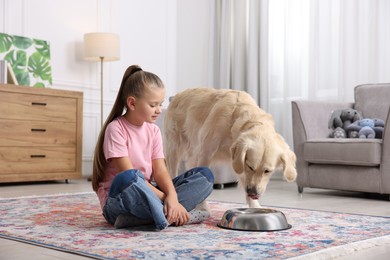 Photo of Girl and her cute Golden Retriever dog drinking water from feeding bowl at home