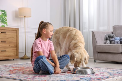 Photo of Girl and her cute Golden Retriever dog near feeding bowl at home