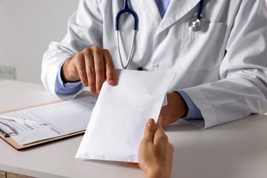 Photo of Corruption concept. Woman giving envelope with money to doctor at white table, closeup