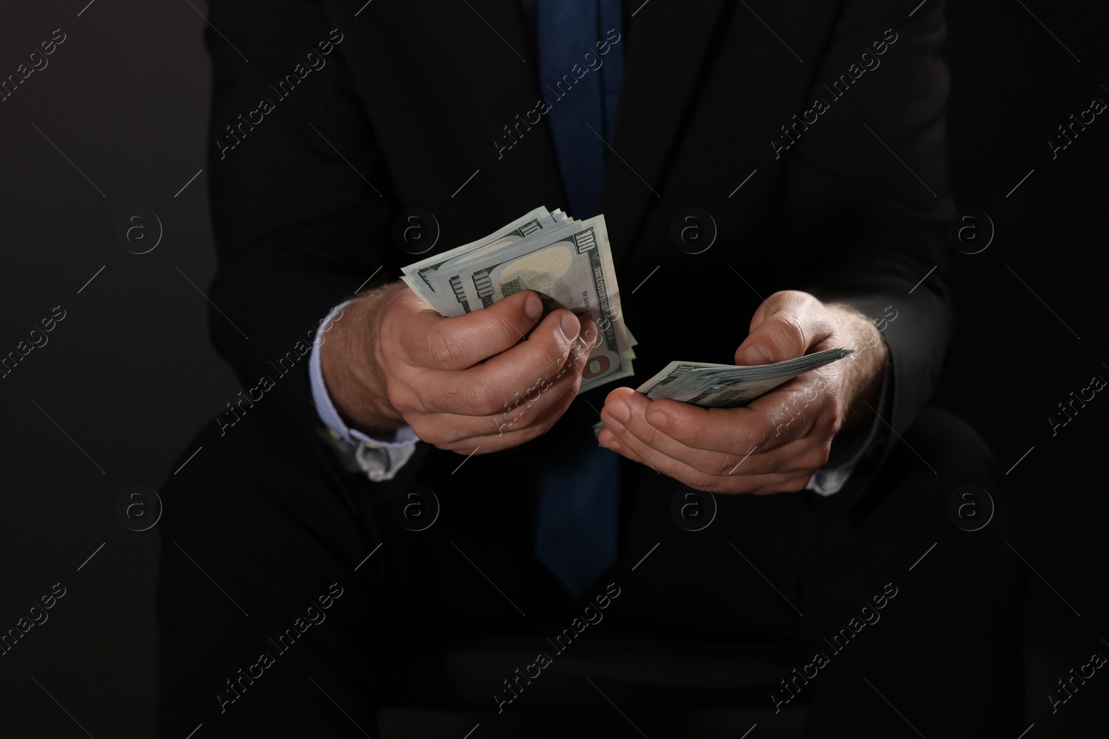 Photo of Corruption concept. Man holding dollar banknotes on black background, closeup