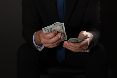 Photo of Corruption concept. Man holding dollar banknotes on black background, closeup