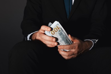 Photo of Corruption concept. Man holding dollar banknotes on black background, closeup