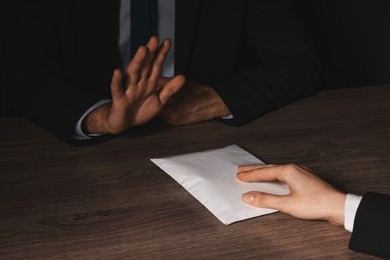 Photo of Corruption concept. Woman giving envelope with money to man at wooden table, closeup