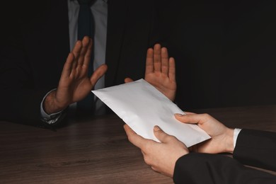 Photo of Corruption concept. Woman giving envelope with money to man at wooden table, closeup