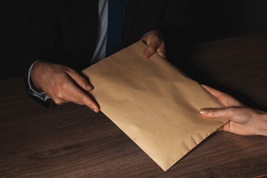 Photo of Corruption concept. Woman giving envelope with money to man at wooden table, closeup