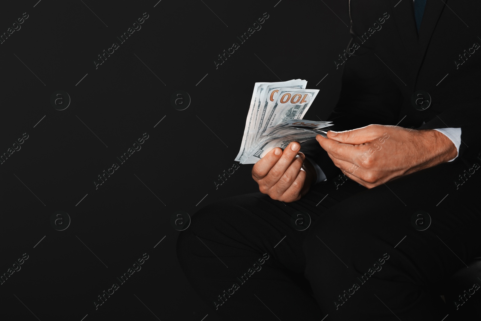 Photo of Corruption concept. Man holding dollar banknotes on black background, closeup. Space for text