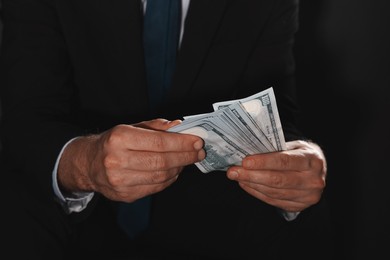 Photo of Corruption concept. Man holding dollar banknotes on black background, closeup