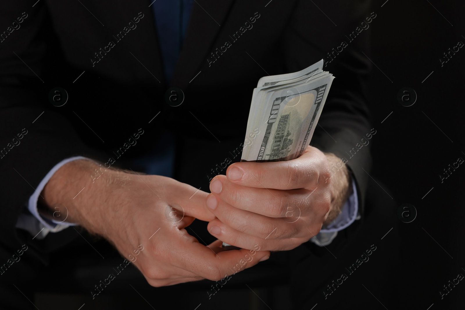 Photo of Corruption concept. Man holding dollar banknotes on black background, closeup