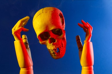 Photo of Human skull and mannequin hands on blue background