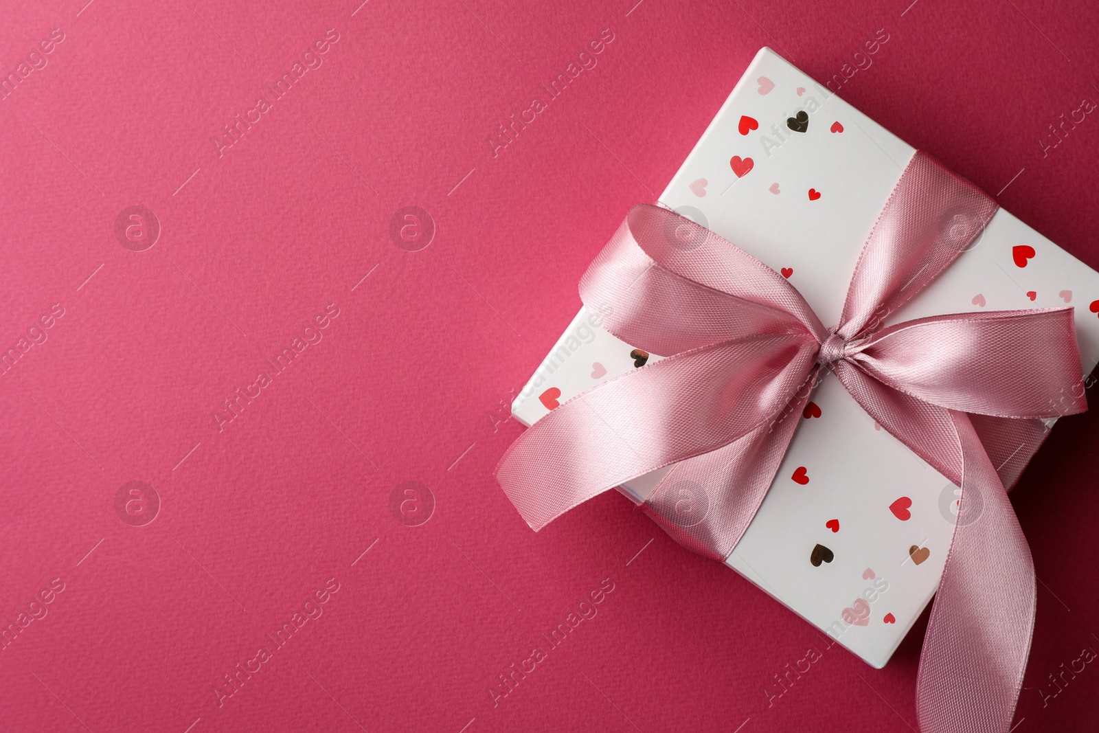 Photo of Beautiful gift box with bow on pink background, top view. Space for text